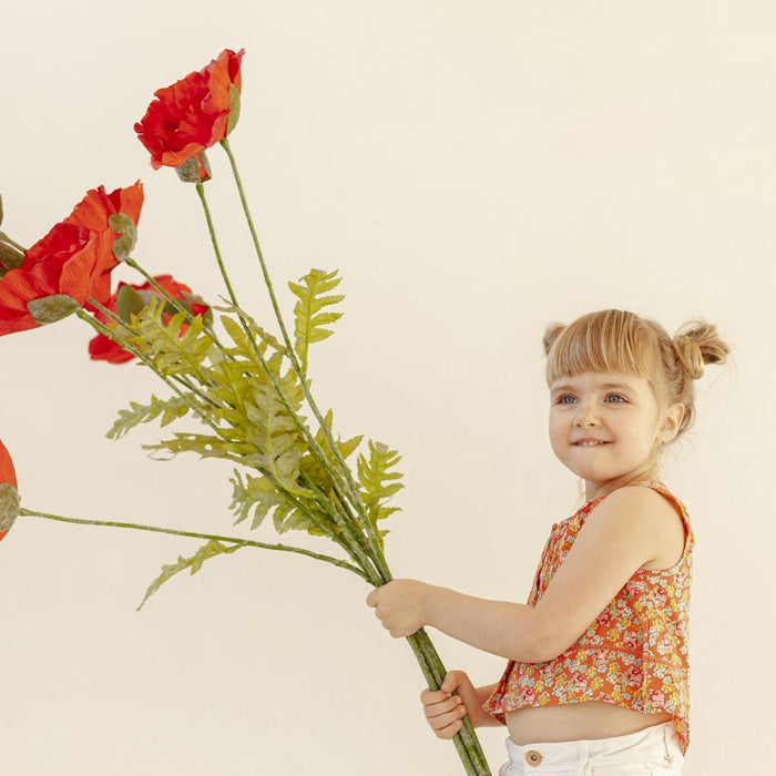 Petite fille portant un grand bouquet de fleurs, ce sont des coquelicots
