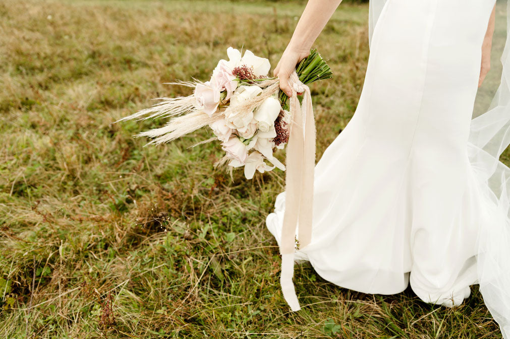Mariée tenant son bouquet de fleurs, champêtre avec petite pampa. Jolie robe longue et blanche.